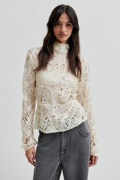 Woman wearing a white lace top and gray jeans on a plain background